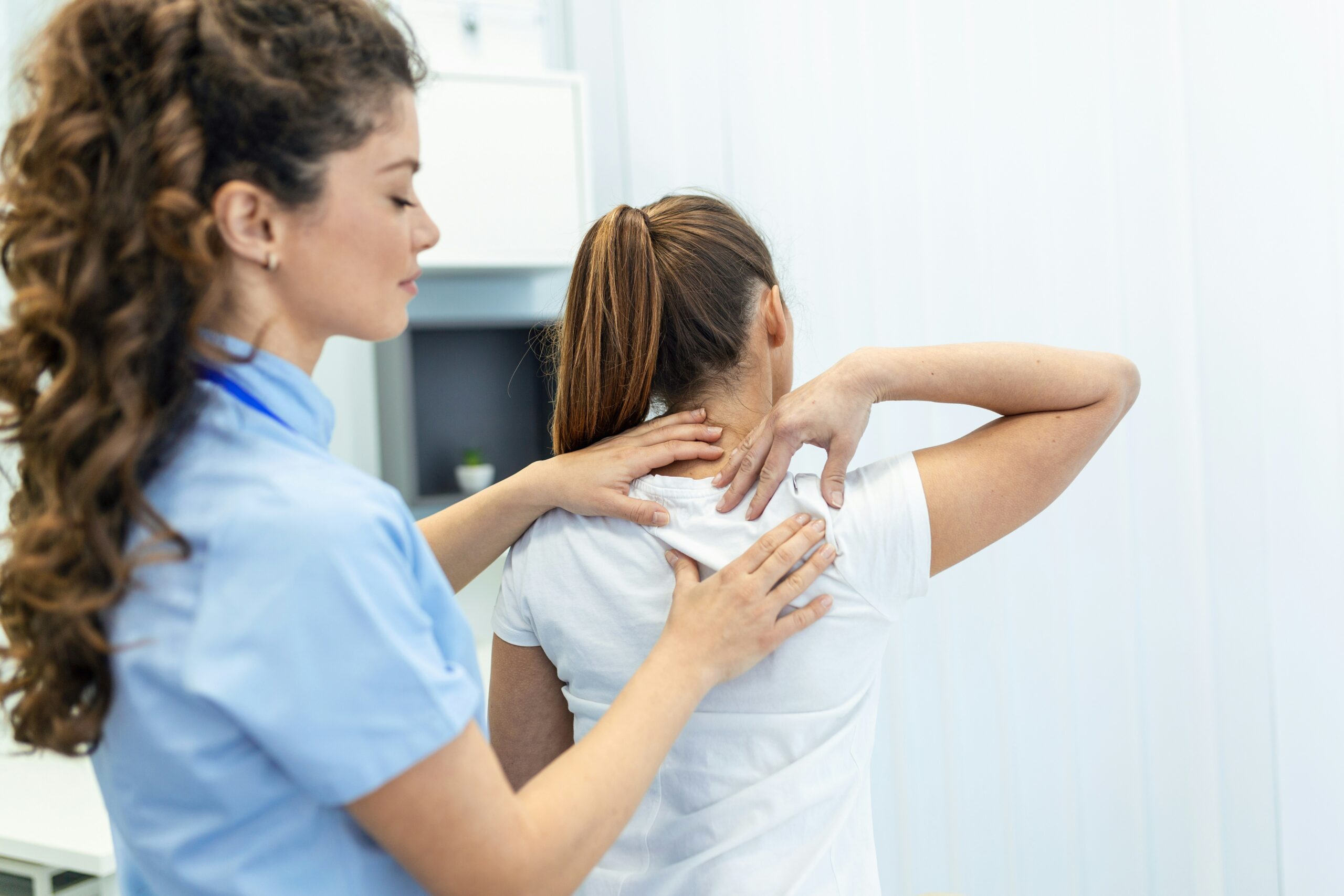 A healthcare professional in examining the neck and upper back area of a patient.